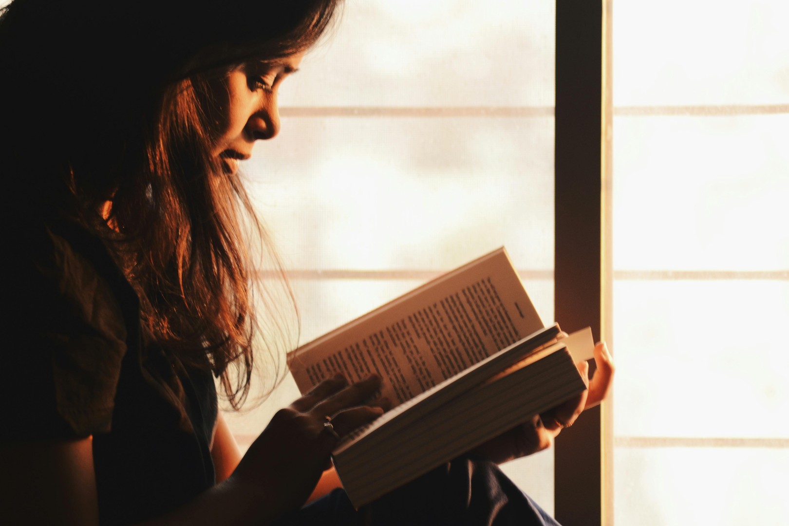 Woman reading book by sunlit window