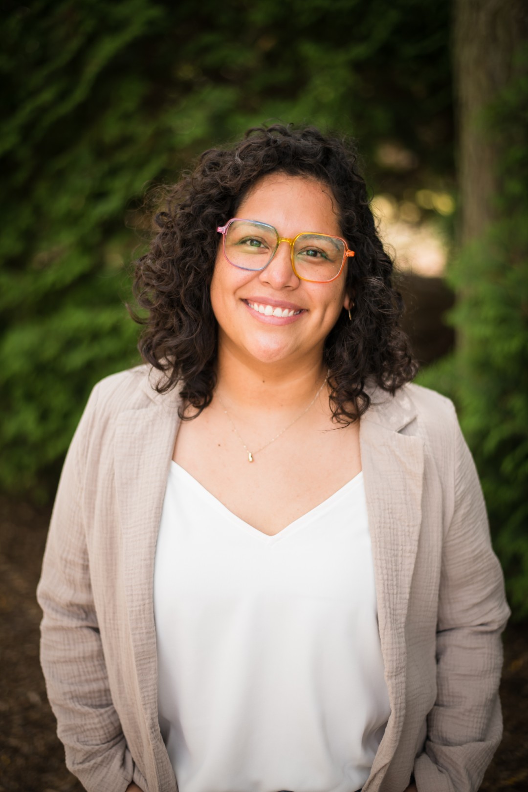 Smiling person in glasses, curly hair, outdoor background.