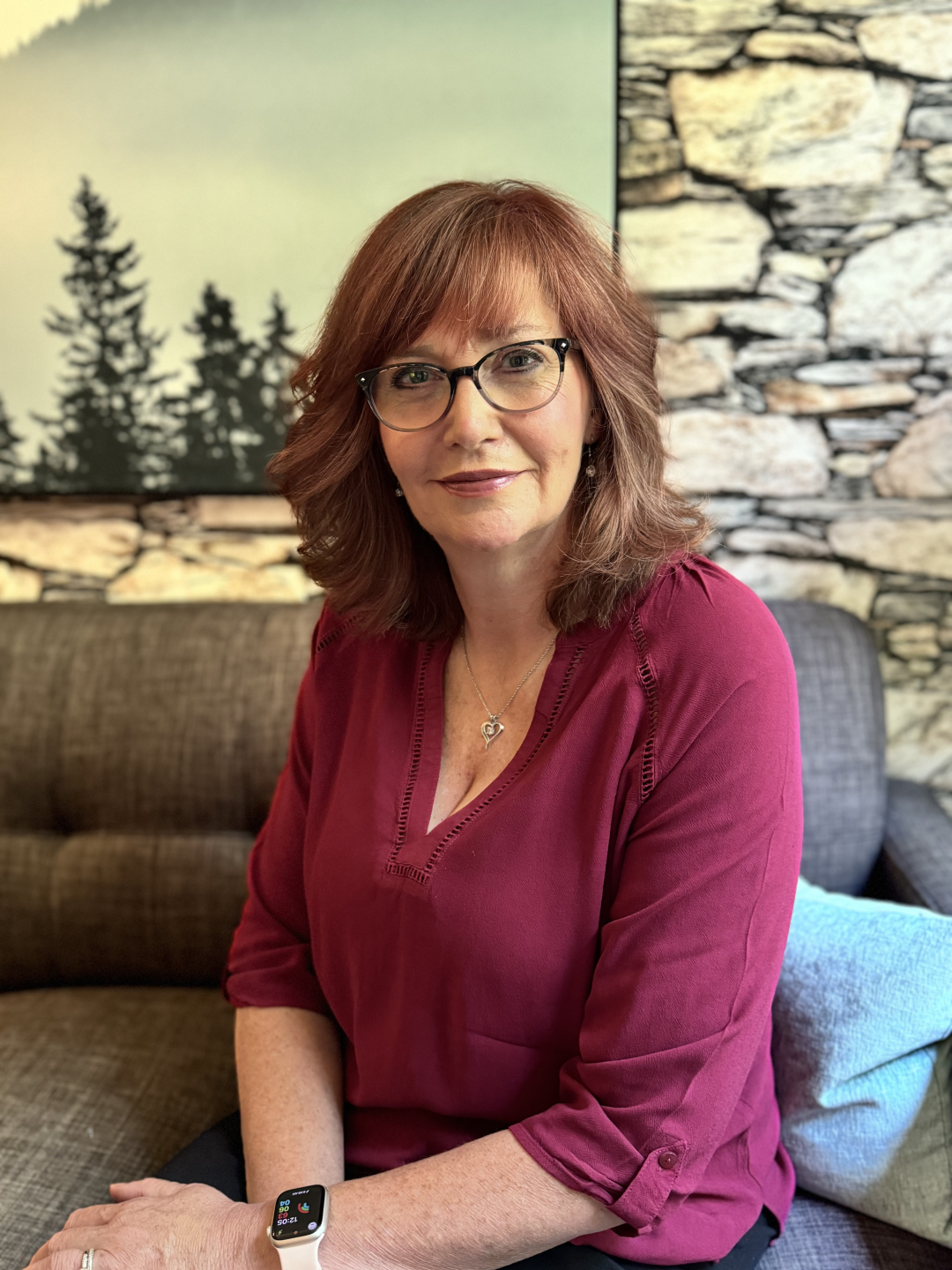 Woman sitting on sofa, wearing glasses and red shirt.