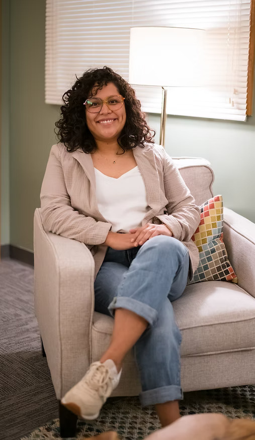 Smiling person sits on armchair in cozy office.
