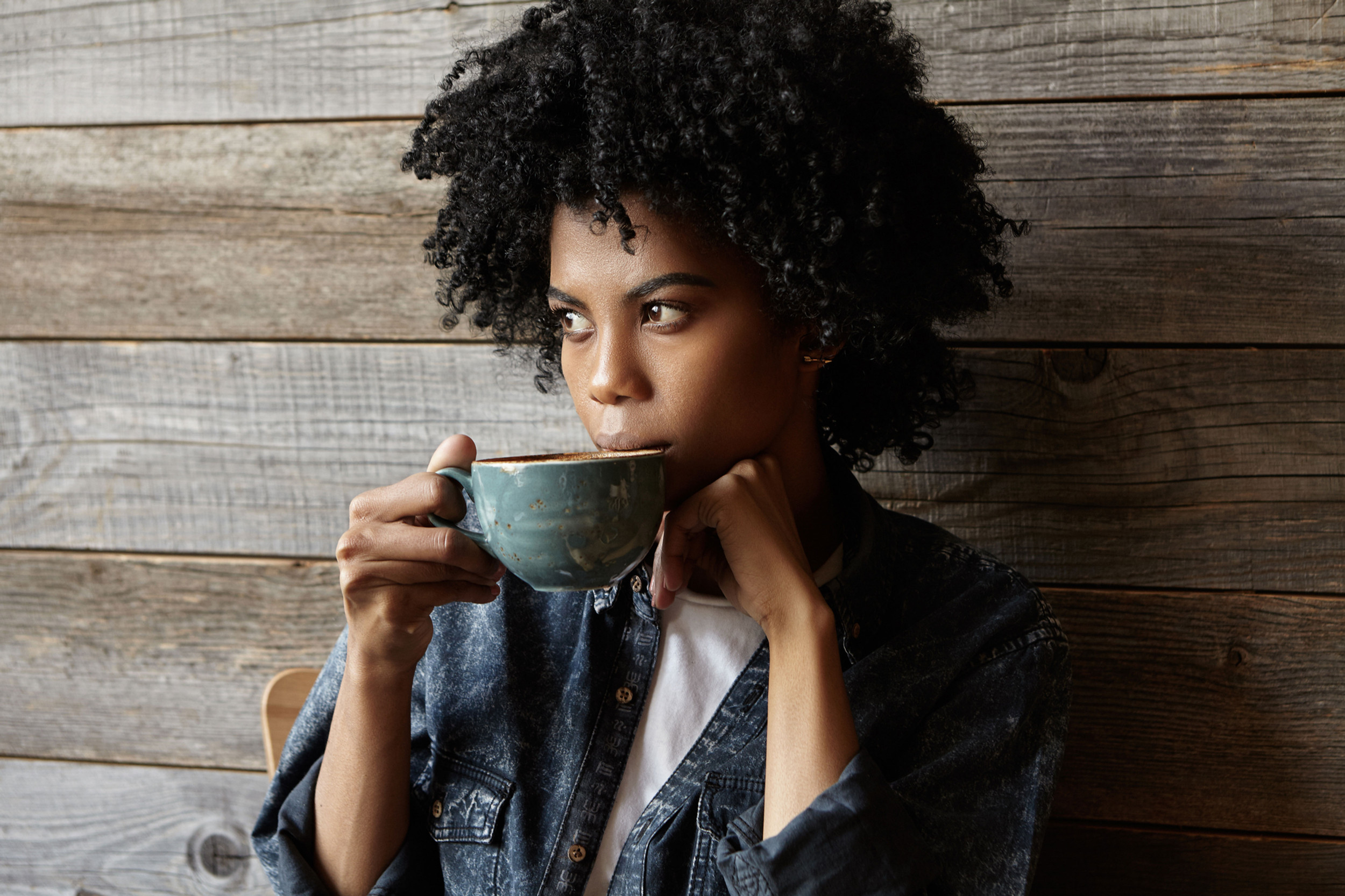 Person enjoying coffee against wooden wall background.