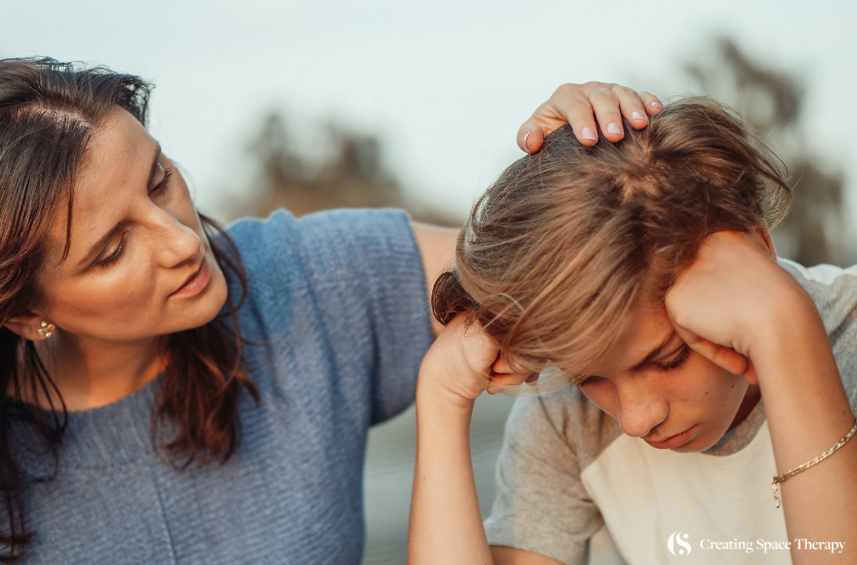 Mother comforts her sad son by gently touching their head.