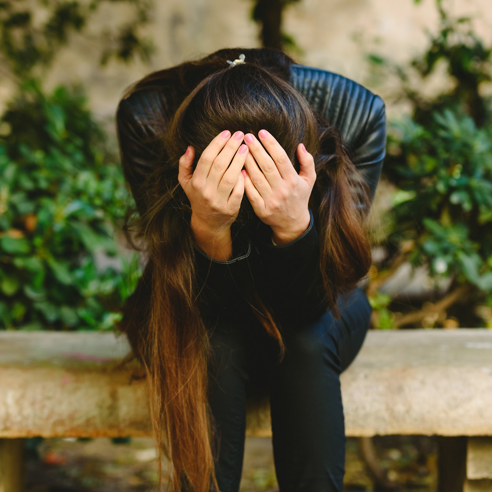 Woman sitting, head in hands, looking distressed.