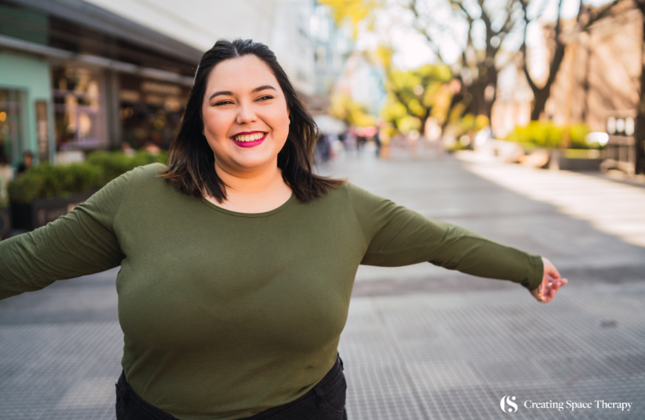 Smiling woman in city street with outstretched arms.