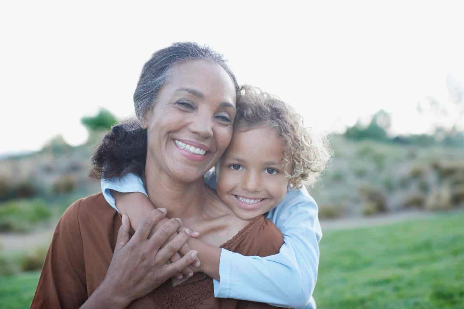 Smiling grandmother and child hugging outdoors.