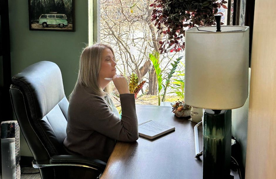 Woman thinking at desk with notebook, window view