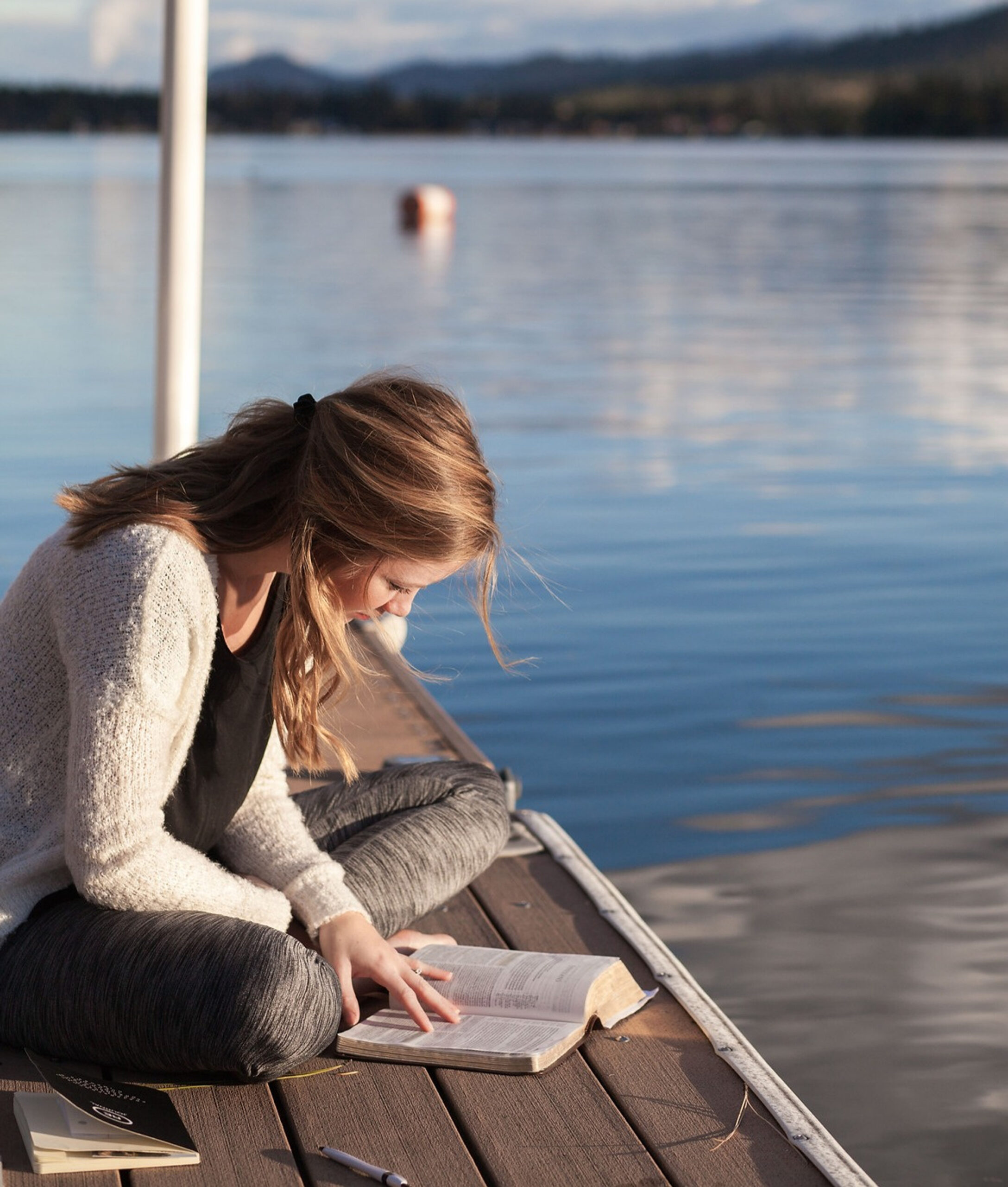 Woman reading book by the lake on dock.